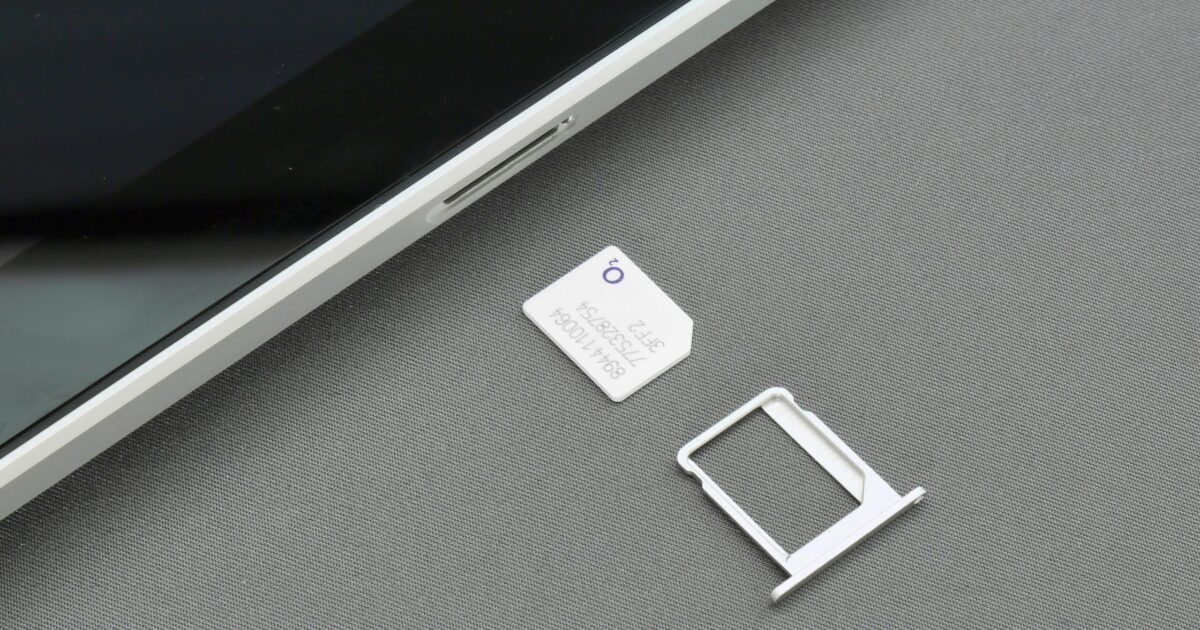 Close-up of a business data SIM card and tray next to a tablet on a grey surface.